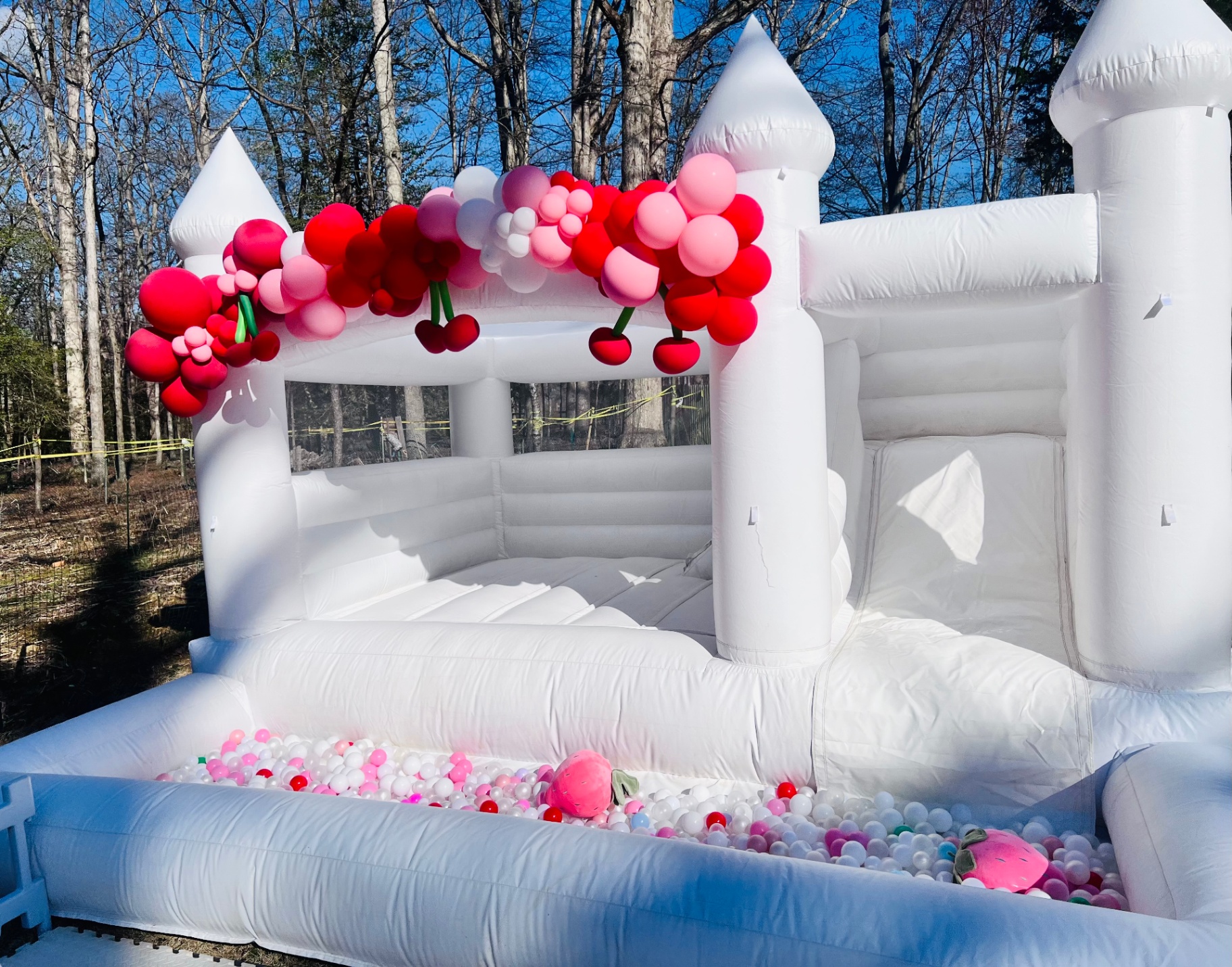 White bounce house with slide, ball pit, and cherry balloon garland